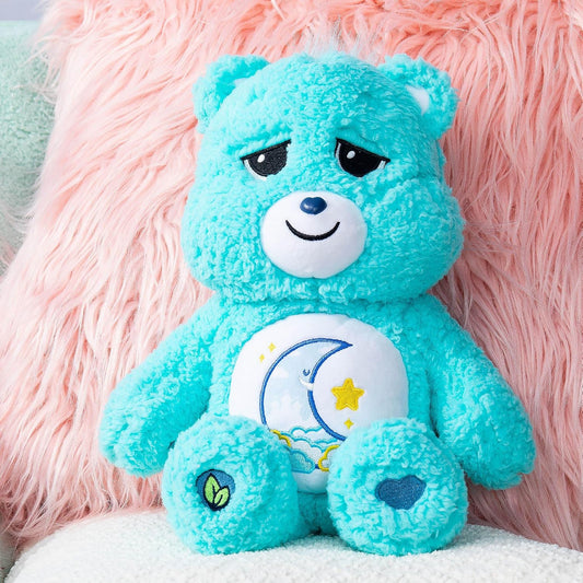 Blue teddy bear with a white belly featuring a moon and star design, sitting against a pink fluffy background.