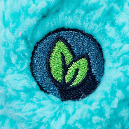 A close-up of a circular embroidered patch featuring two bright green leaves on a dark blue and black background, placed on a textured turquoise fabric surface.