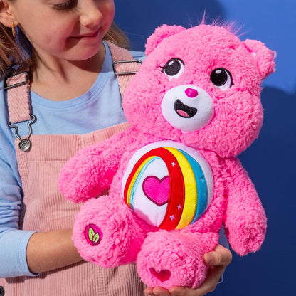 Child holding a pink teddy bear with a rainbow and heart design against a blue background