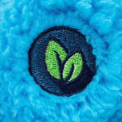 A close-up of a textured bright blue fuzzy fabric with a circular embroidered patch featuring two green leaves inside a dark navy circle.