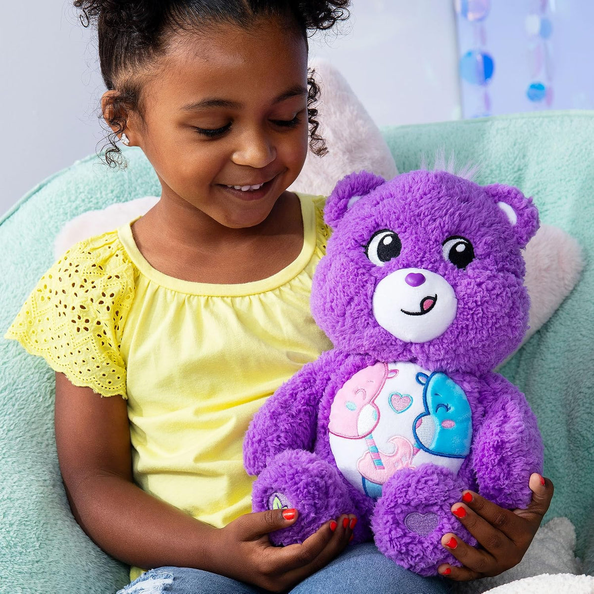 Young girl holding a purple teddy bear with a heart design on a light green couch.