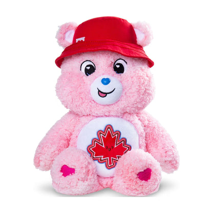 A pink plush teddy bear wearing a red bucket hat and a white belly patch with a red maple leaf, photographed on a clean white background.