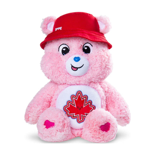 A pink plush teddy bear wearing a red bucket hat and a white belly patch with a red maple leaf, photographed on a clean white background.