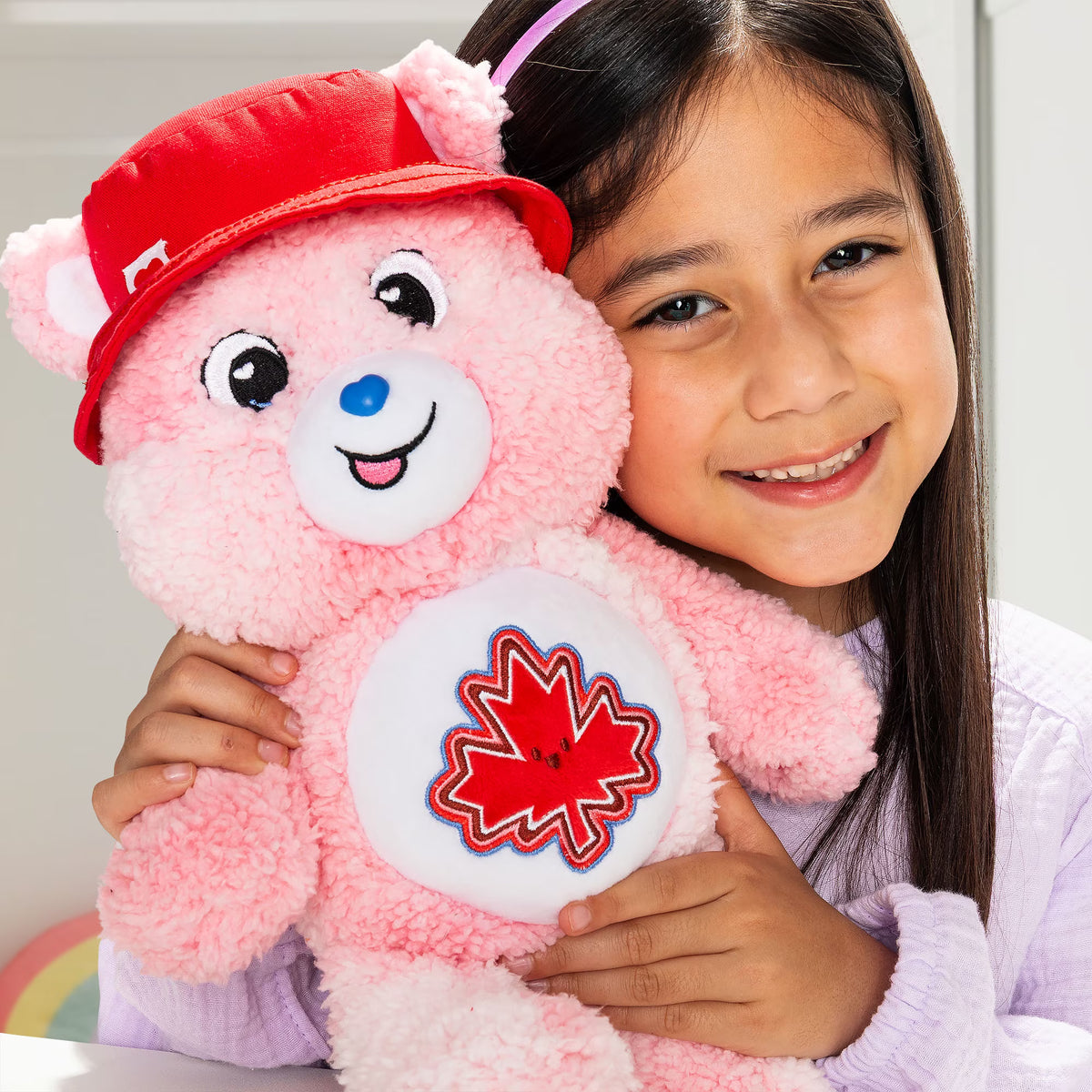 Child holding a pink teddy bear with a red maple leaf design