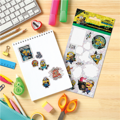 Minion-themed stickers on a sheet with stationery items on a wooden surface