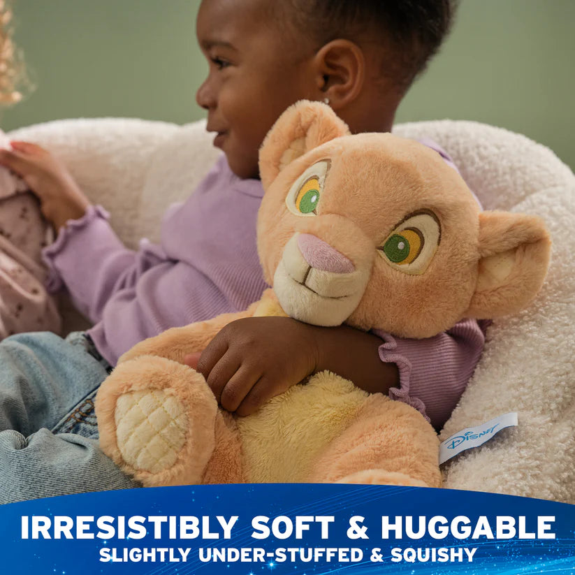 Child holding a plush lion toy with Disney branding, sitting on a soft surface.