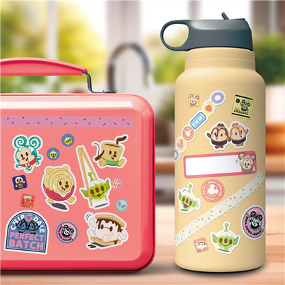 Pink lunch box and beige water bottle with cartoon character stickers on a blurred background
