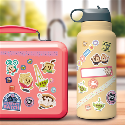 Pink lunch box and beige water bottle with cartoon character stickers on a blurred background