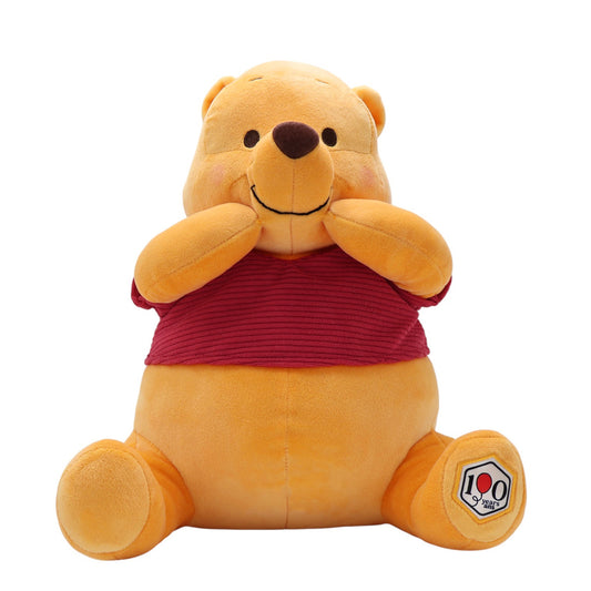 Disney Winnie the Pooh 100th Anniversary Pooh plush, sitting with paws on cheeks, wearing a red corduroy shirt with a 100 Years patch.