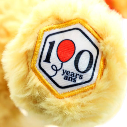 Close-up of a plush toy with a '100 years ans' patch on a white background