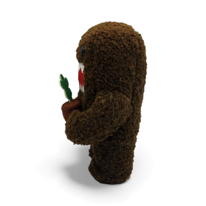 Side view of the 6.5-inch Domo plush, a brown fuzzy monster holding a small
brown pot with a yellow flower.