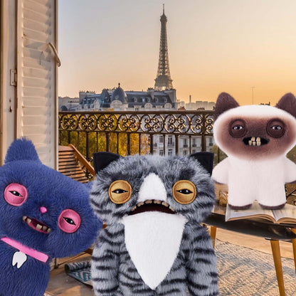 Three Fuggler Alley Cat plush toys in front of a balcony with the Eiffel Tower in the background.