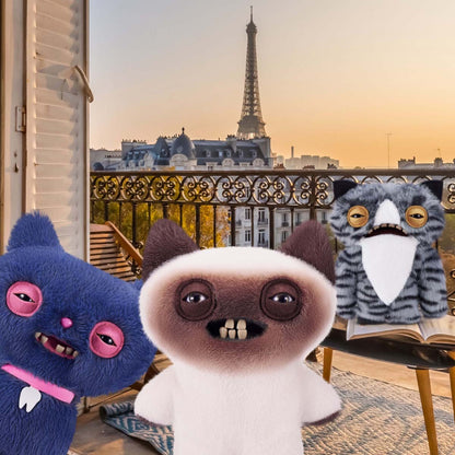 Three Fuggler Alley Cat plush toys in front of a balcony with the Eiffel Tower in the background.