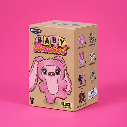 A cardboard mystery box for 'Fuggler's Baby Baddies' plush bag charms, featuring a pink bunny illustration on the front, set against a solid pink background.