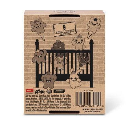 Back of display box for A small, yellowish-beige Fuggler Baby Fugg plush toy (Screech) with large green eyes, one white baby tooth showing in a pink mouth, and a spiky brown tuft of hair on top.