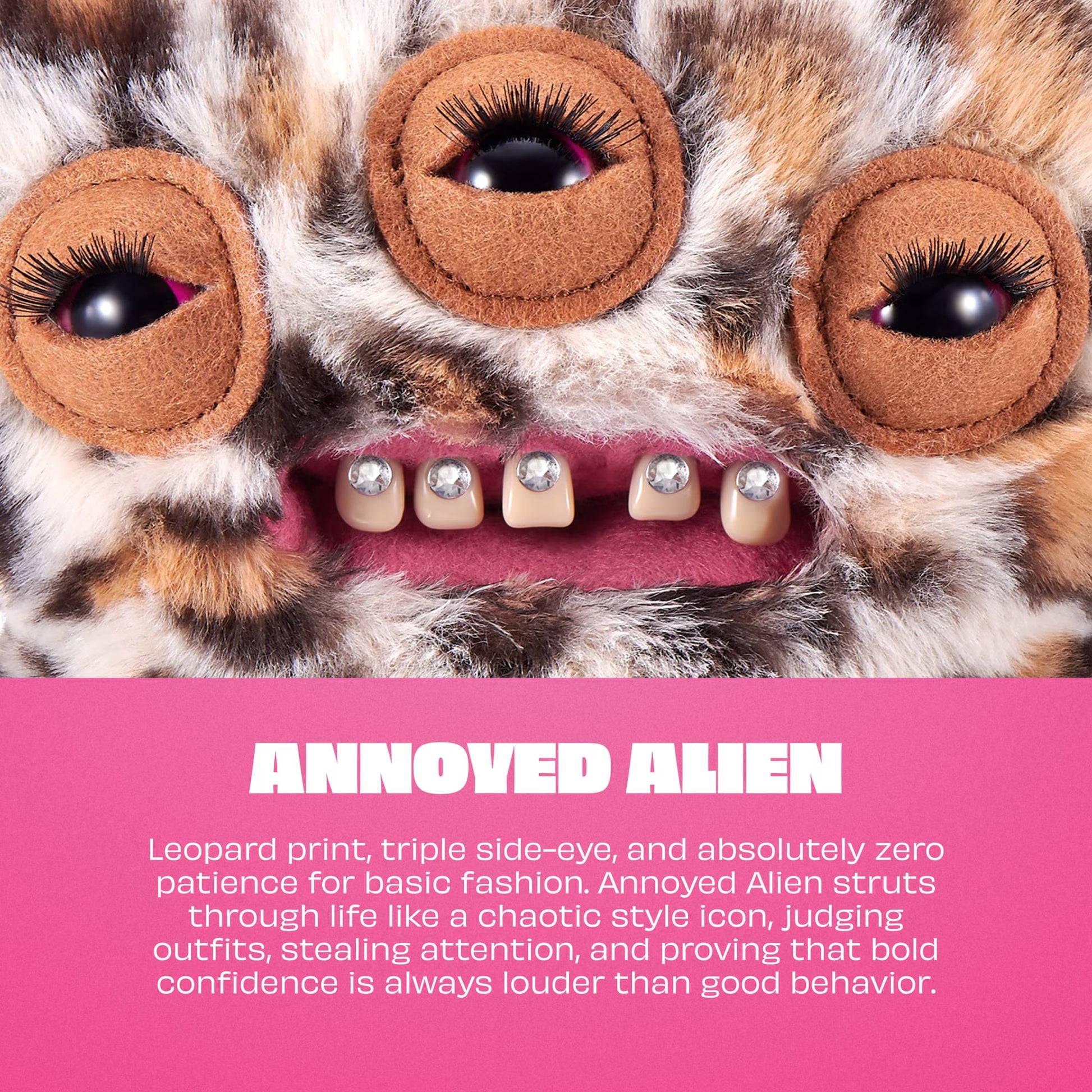 A close-up of a plush leopard-print monster face with three large embroidered side-eyes and a stitched mouth showing silver tooth-like teeth. A pink text band at the bottom reads 'ANNOYED ALIEN' with descriptive copy.
