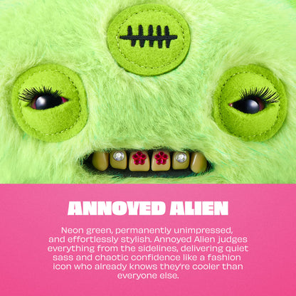 A neon green fuzzy monster face with large embroidered eyes, black eyelashes, a stitched scar patch on the forehead, and a row of teeth with rhinestones and red flower accents. A pink text band at the bottom reads 'ANNOYED ALIEN' with descriptive copy.