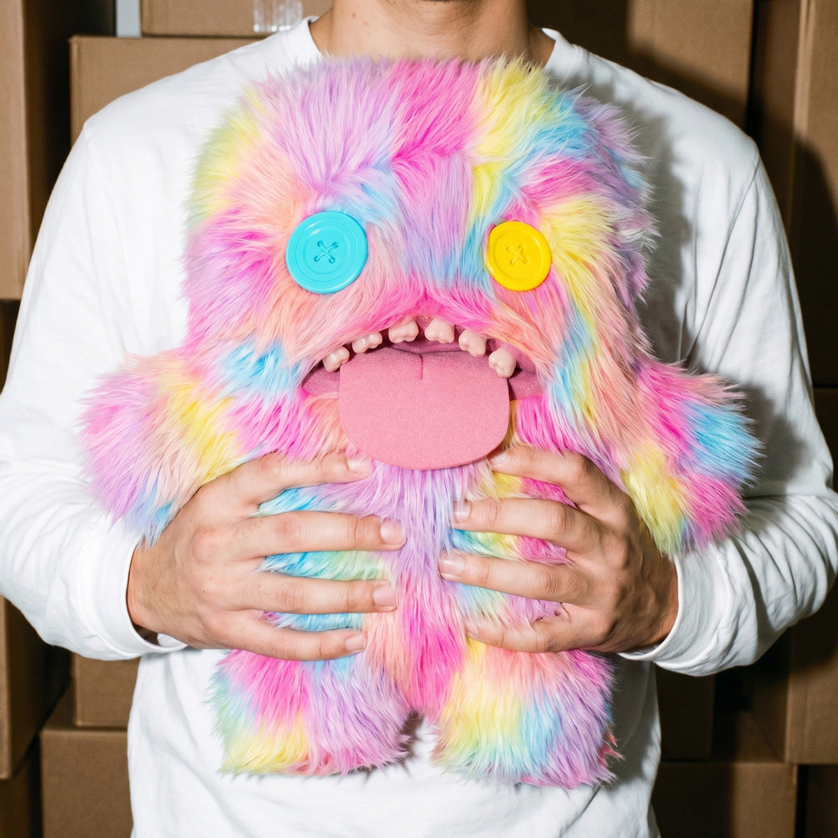 Person holding a Fuggler Bigg Fugg Oogah Boogah 18-Inch Plush featuring pastel tie-dye fur, mismatched button eyes, a pink tongue, and human-like teeth.