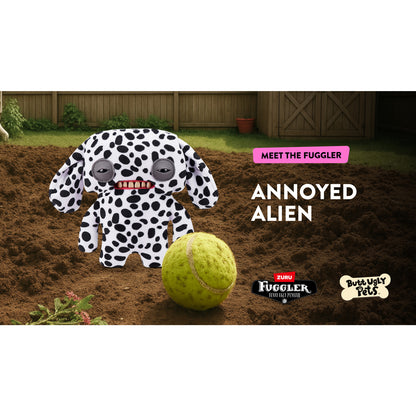 A 9-inch Fuggler Butt Ugly Pet (Annoyed Alien Dalmatian) plush toy. It has white fabric with black Dalmatian spots, long floppy ears, squinting grey eyelids, and a mouth with realistic human teeth. It is on a dug out grass landscape with a tennis ball and "Meet the Fuggler" and Zuru brandings text. 
