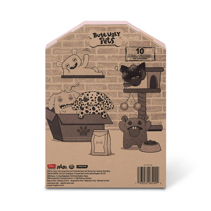 Back of display box for A 9-inch Fuggler Butt Ugly Pet (Cheeky Chonky Guinea Pig) plush toy. It has shaggy rainbow-colored fur, pointy purple ears, squinting purple eyelids, two human-like teeth, and a large pink felt tongue sticking out.