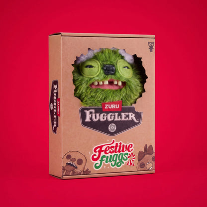A cardboard display box for the Zuru Fuggler, featuring a cutout window that reveals a green furry monster head with a black nose and teeth. The box is decorated with 'ZURU FUGGLER' and 'Festive Fuggs' text, set against a solid red background.