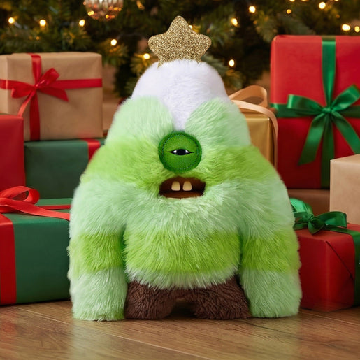 Fuggler Festive Fuggs Series 2 Sasquooshmas Tree 9-inch green tree-shaped plush with a single cyclops eye, gold star, and human-like teeth., posed in front of wrapped Christmas presents on a wooden floor.