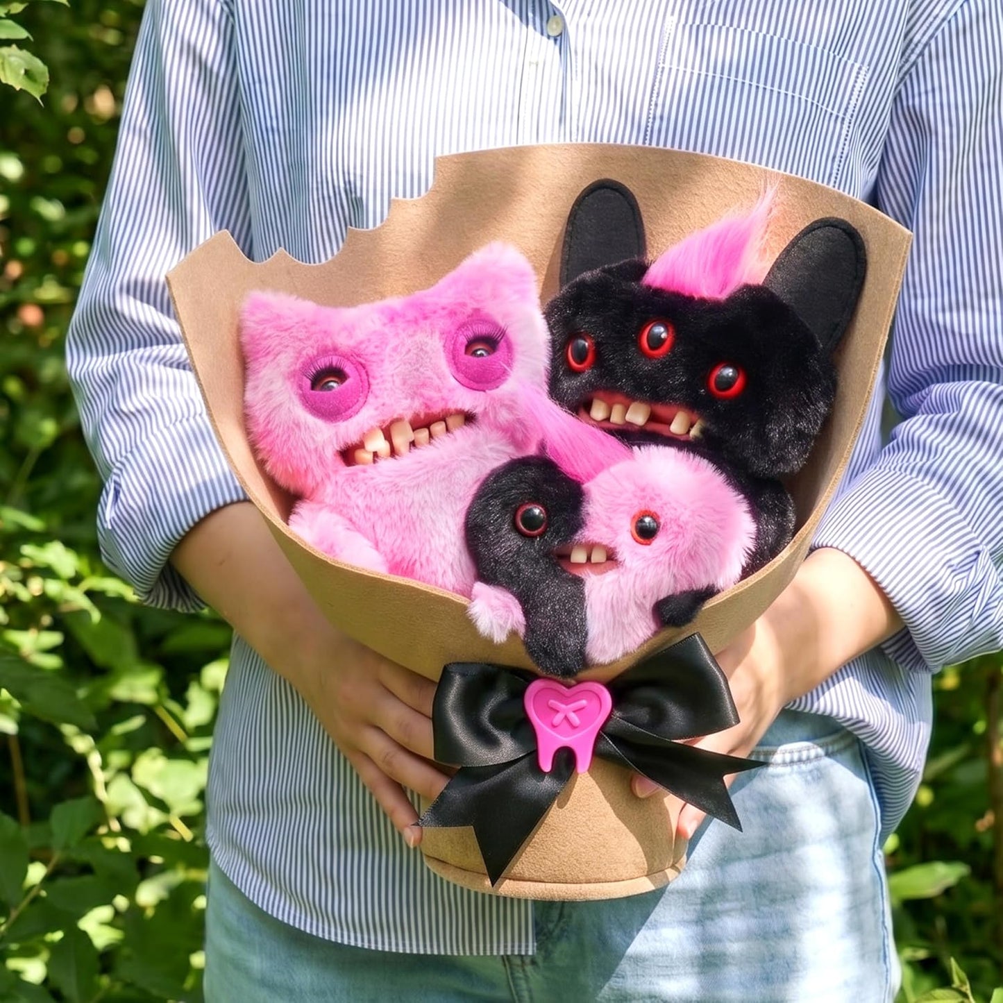 Bouquet of pink and black plush toys resembling monsters held by a person outdoors.