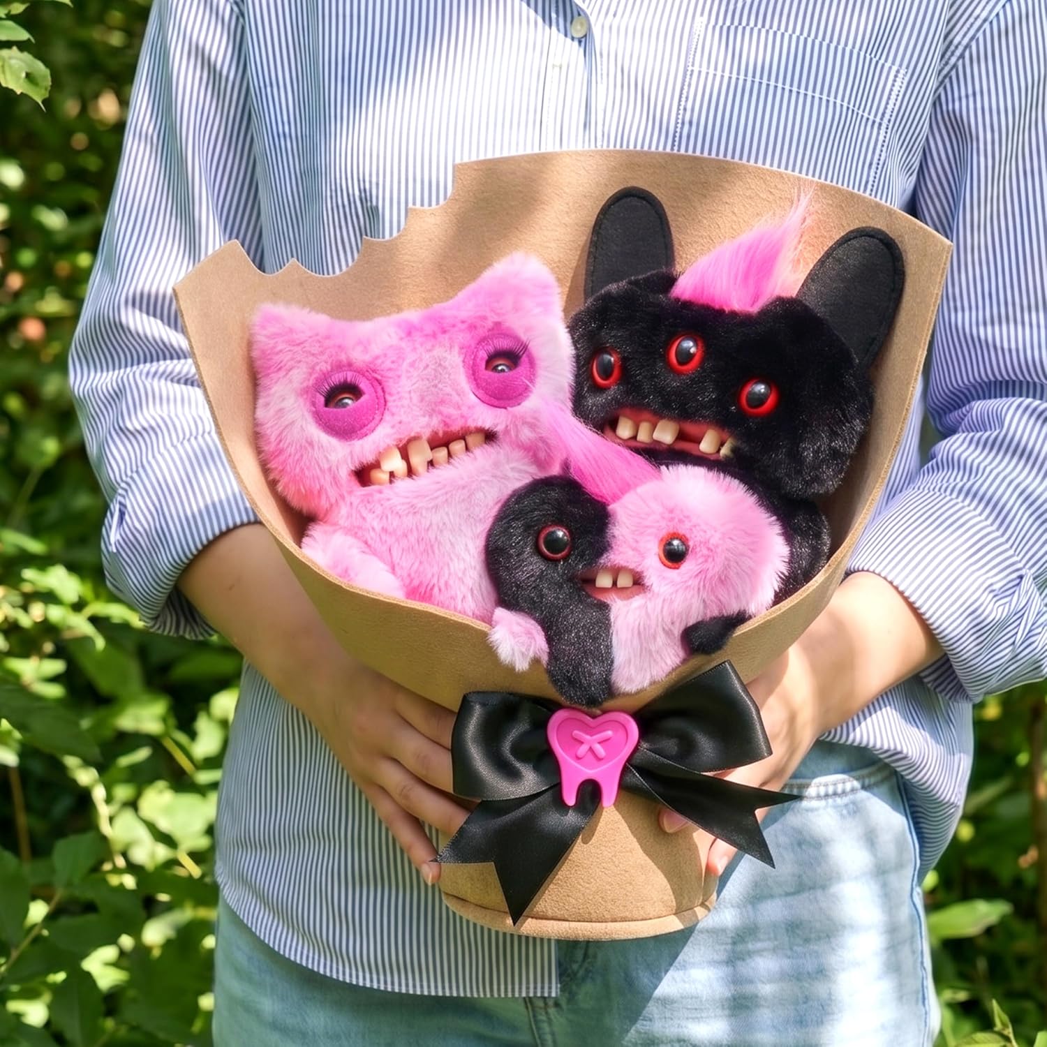 Bouquet of pink and black plush toys resembling monsters held by a person outdoors.