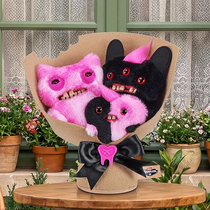 Fuggler Fugg Bouquets Plush Set featuring two 9-inch and one 3.5-inch pink and black monster plush toys wrapped in craft paper with a black ribbon. with plants in the background