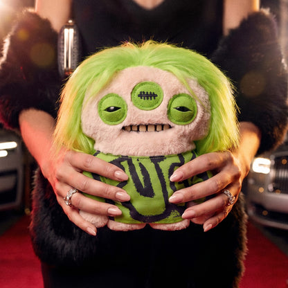 Person holding a green and yellow plush toy with a unique design on a red carpet.
