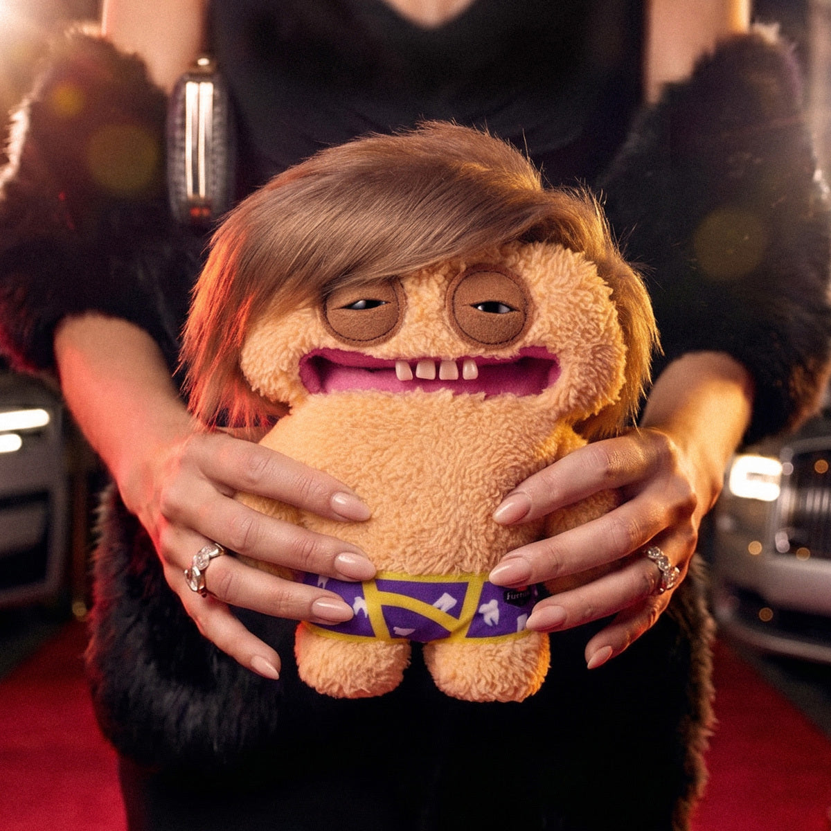 Person holding a plush toy with a unique design on a red carpet
