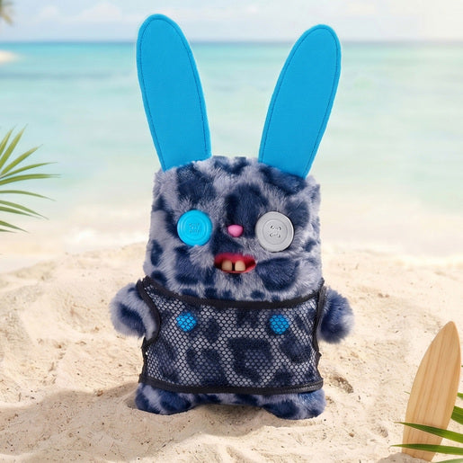 Fuggler Nipple Fuggs Rabid Rabbit plush toy with blue leopard print fur, tall blue ears, wearing a black mesh shirt, featuring mismatched button eyes and human-like buck teeth on a beach