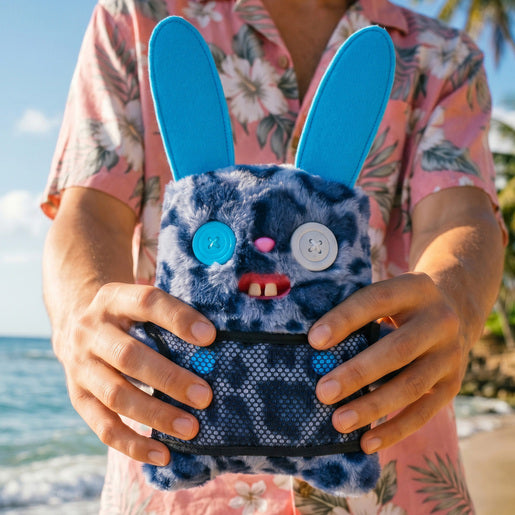 Person holding Fuggler Nipple Fuggs Rabid Rabbit plush toy with blue leopard print fur, tall blue ears, wearing a black mesh shirt, featuring mismatched button eyes and human-like buck teeth.