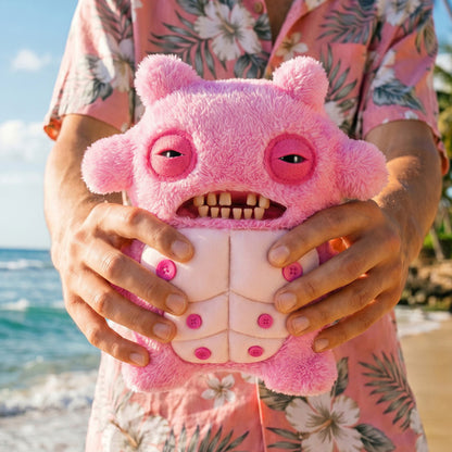 Person holding a Fuggler Nipple Fuggs Sir Nobbynuts plush toy in fluffy bubblegum pink with human-like teeth, half-closed eyes, and six pink buttons on its belly