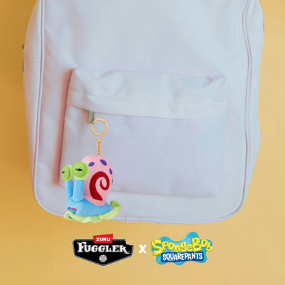 Backpack with a colorful character keychain on a yellow background, featuring Zuru Fuggler and SpongeBob SquarePants logos.