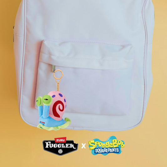 Backpack with a colorful character keychain on a yellow background, featuring Zuru Fuggler and SpongeBob SquarePants logos.