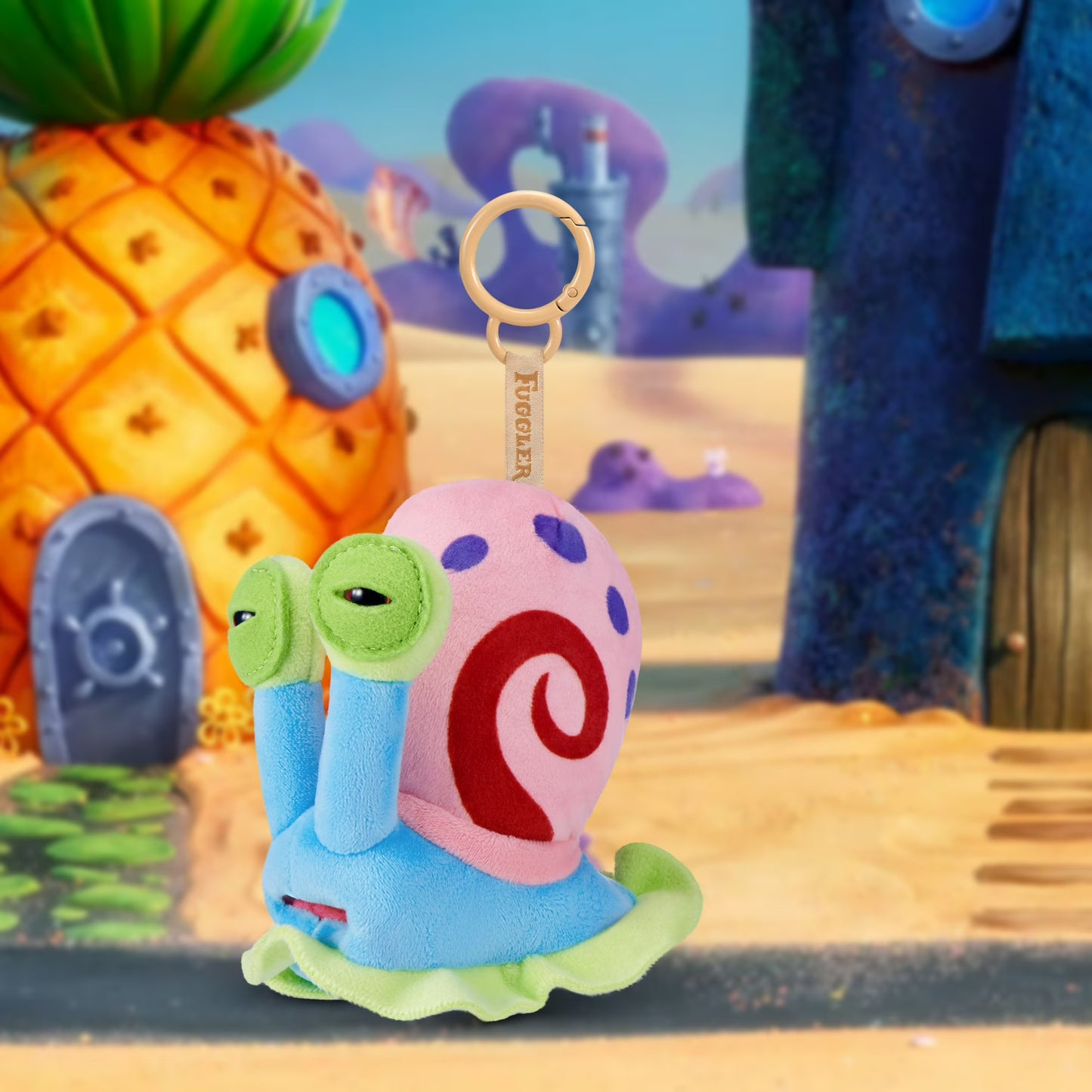 Plush toy keychain with a colorful design in front of a pineapple house and tree.