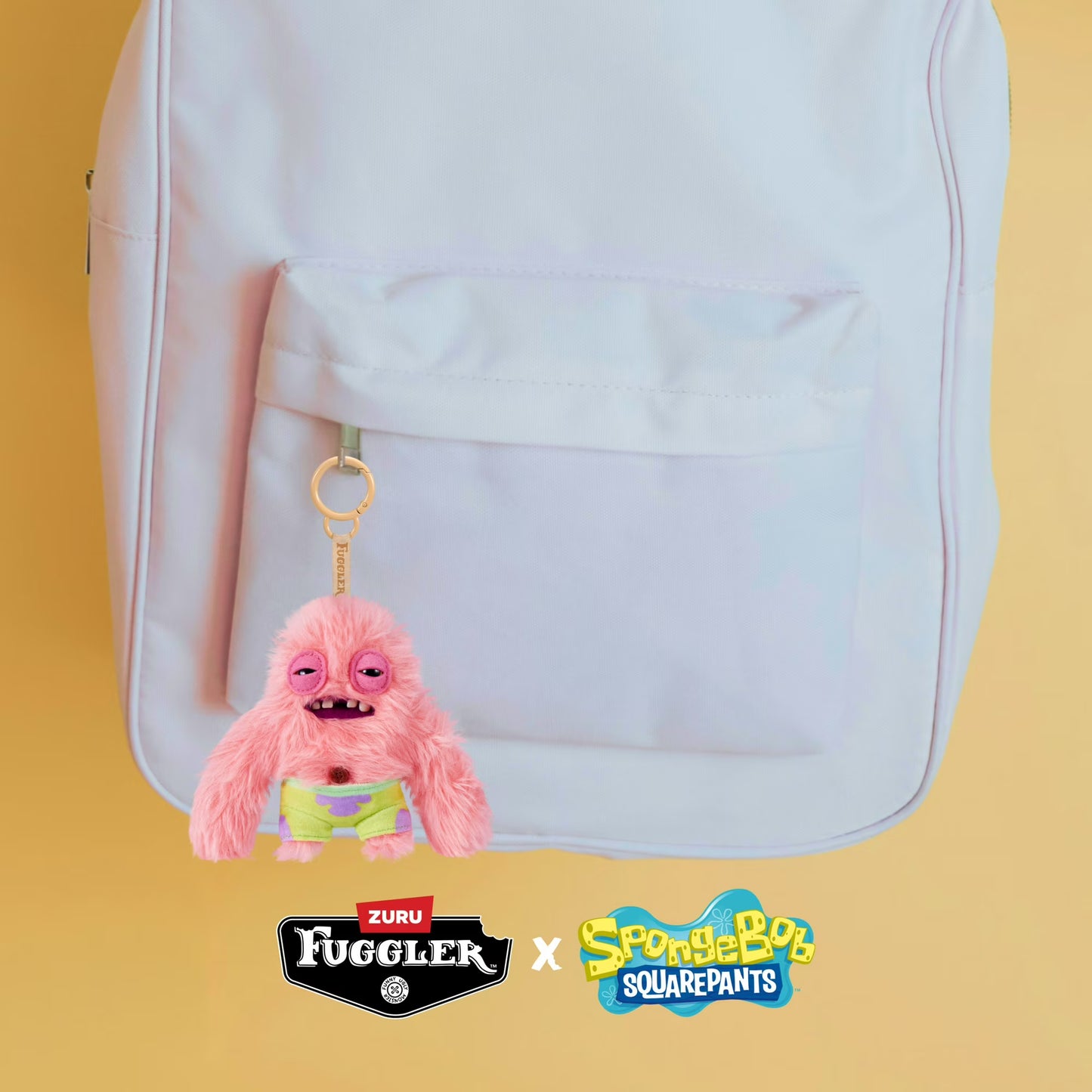 Pink plush keychain with a yellow tag attached to a white backpack on a yellow background, featuring Fuggler and SpongeBob SquarePants logos.