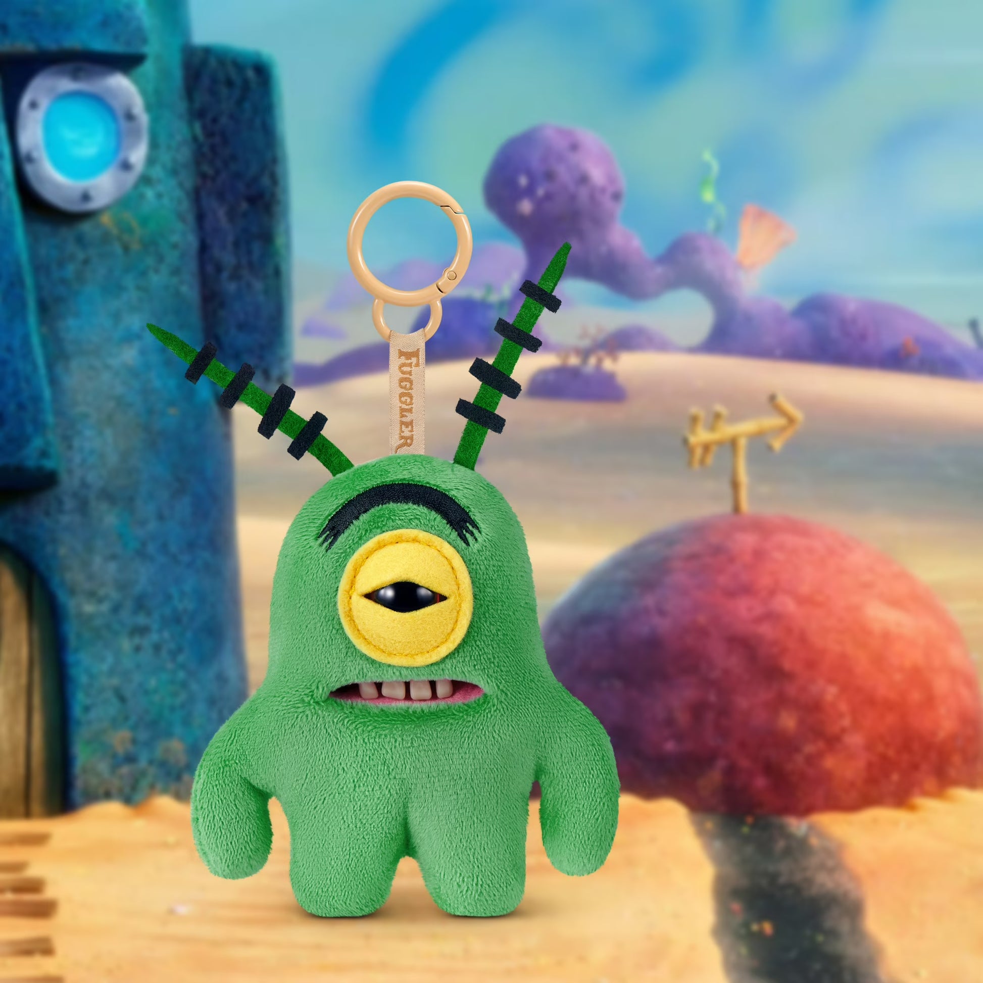 Green plush toy with one eye and antenna keychain against a colorful, cartoon-like background