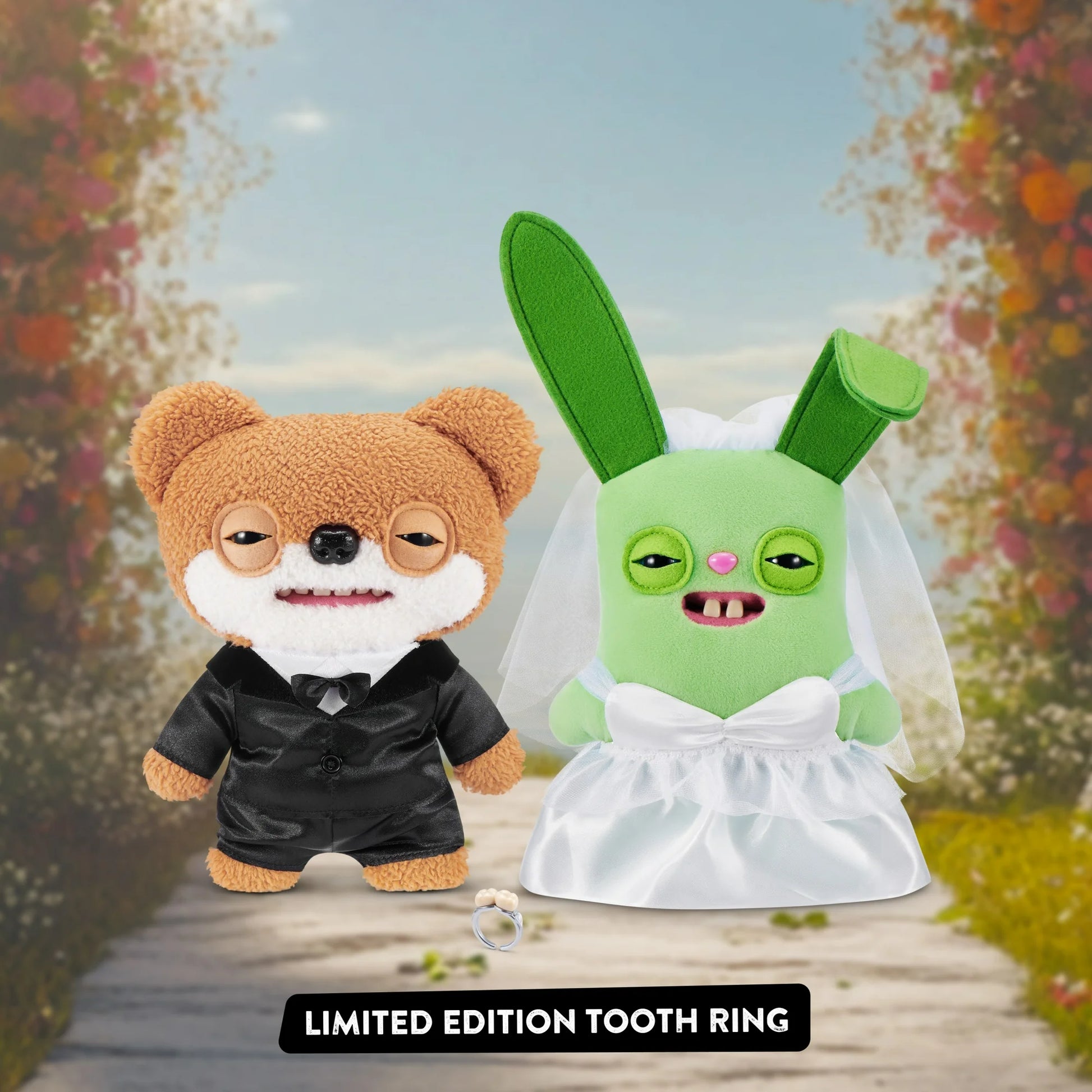 Two plush toys, one brown and one green, standing on a wooden path with a floral background. A limited edition tooth ring is displayed below them.
