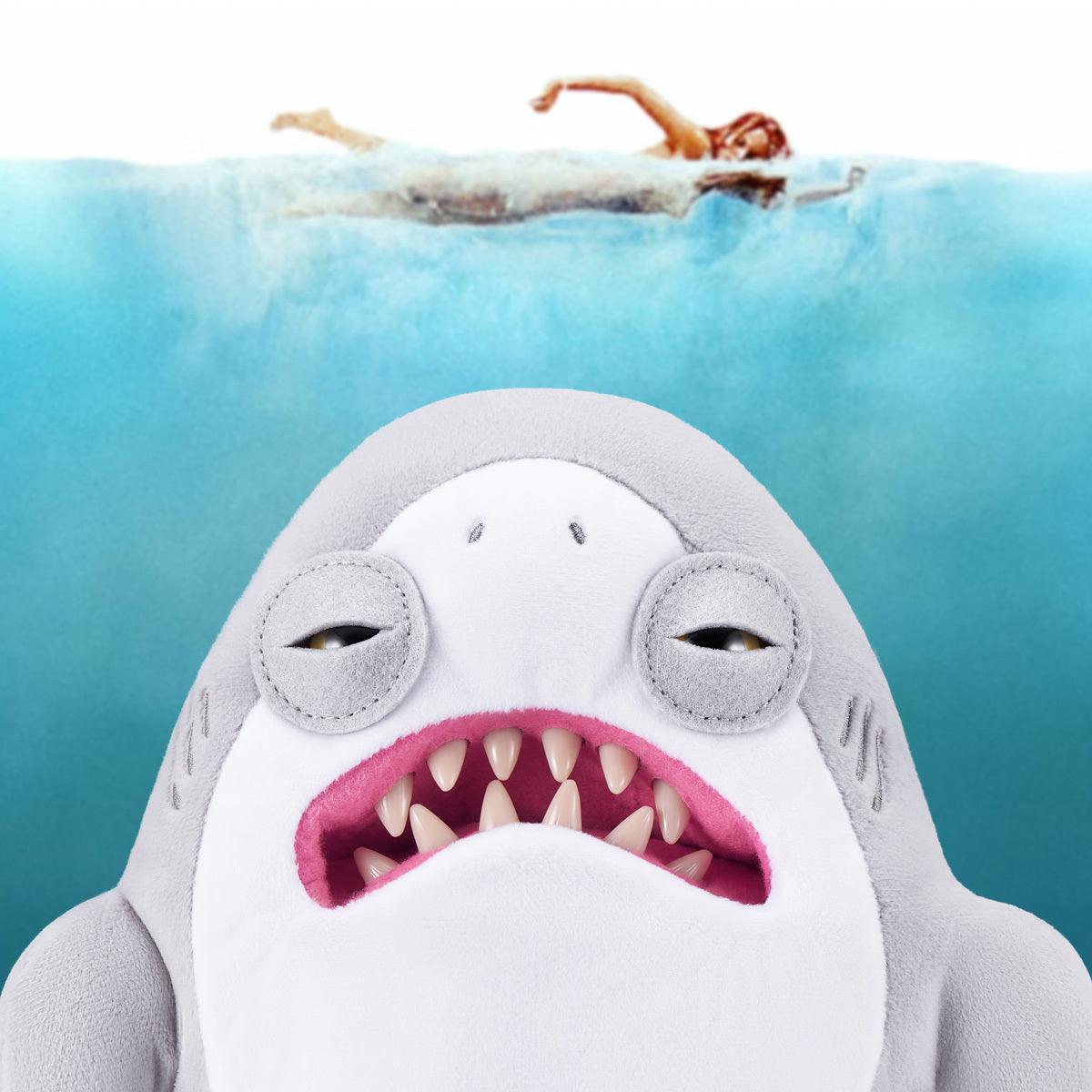 A humorous promotional image showing the Jaws Fuggler lurking underwater beneath a swimmer, recreating the iconic movie poster scene with a funny twist.