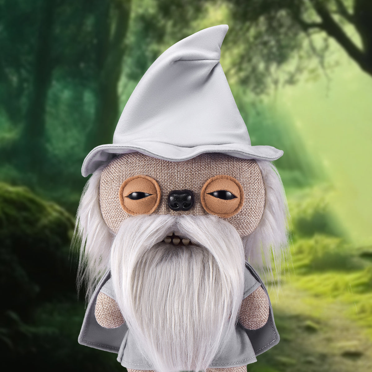 The Gandalf Fuggler plush toy displayed against a Lord of the Rings inspired forest background, emphasizing his grey robes and mischievous expression.