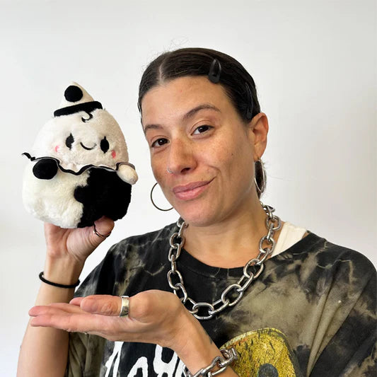 Person holding a plush toy resembling a black and white character with a hat against a plain background