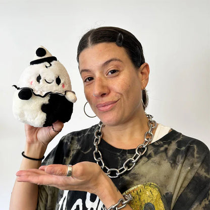 Person holding a plush toy resembling a black and white character with a hat against a plain background