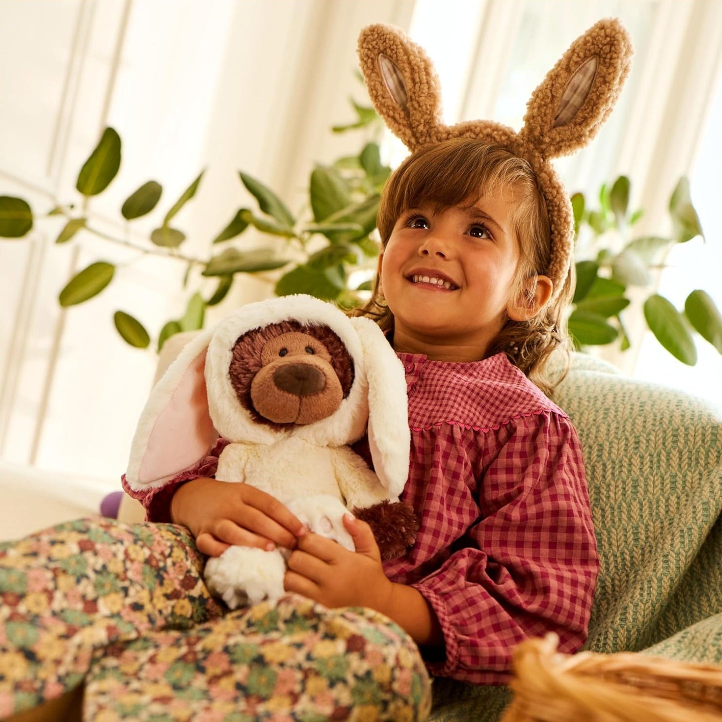 Child wearing bunny ears holding a teddy bear in a cozy indoor setting