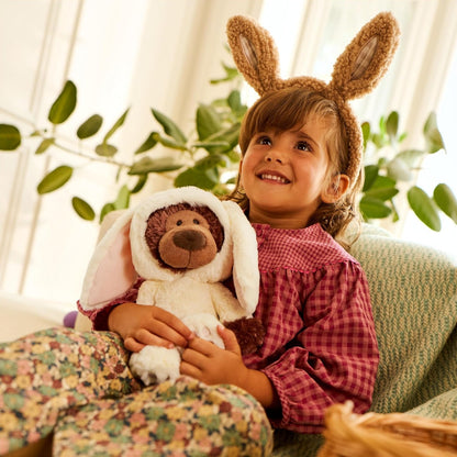 Child wearing bunny ears holding a teddy bear in a cozy indoor setting