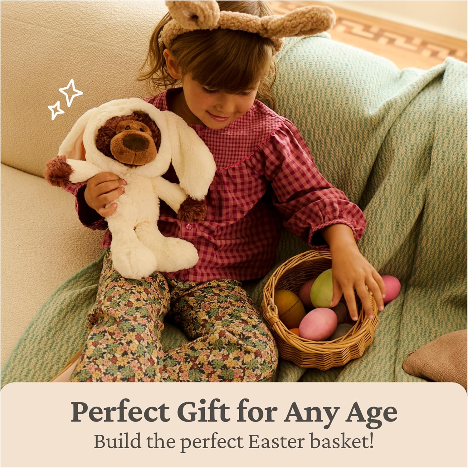 Child holding a GUND Philbin 7-inch chocolate-brown teddy bear wearing a cream-colored bunny costume with floppy ears and a basket of Easter eggs on a couch, with text 'Perfect Gift for Any Age' and 'Build the perfect Easter basket!'.