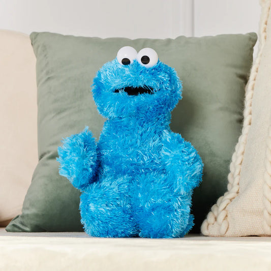 GUND Sesame Street Cookie Monster 12-inch plush toy sitting on a couch with green and beige pillows.