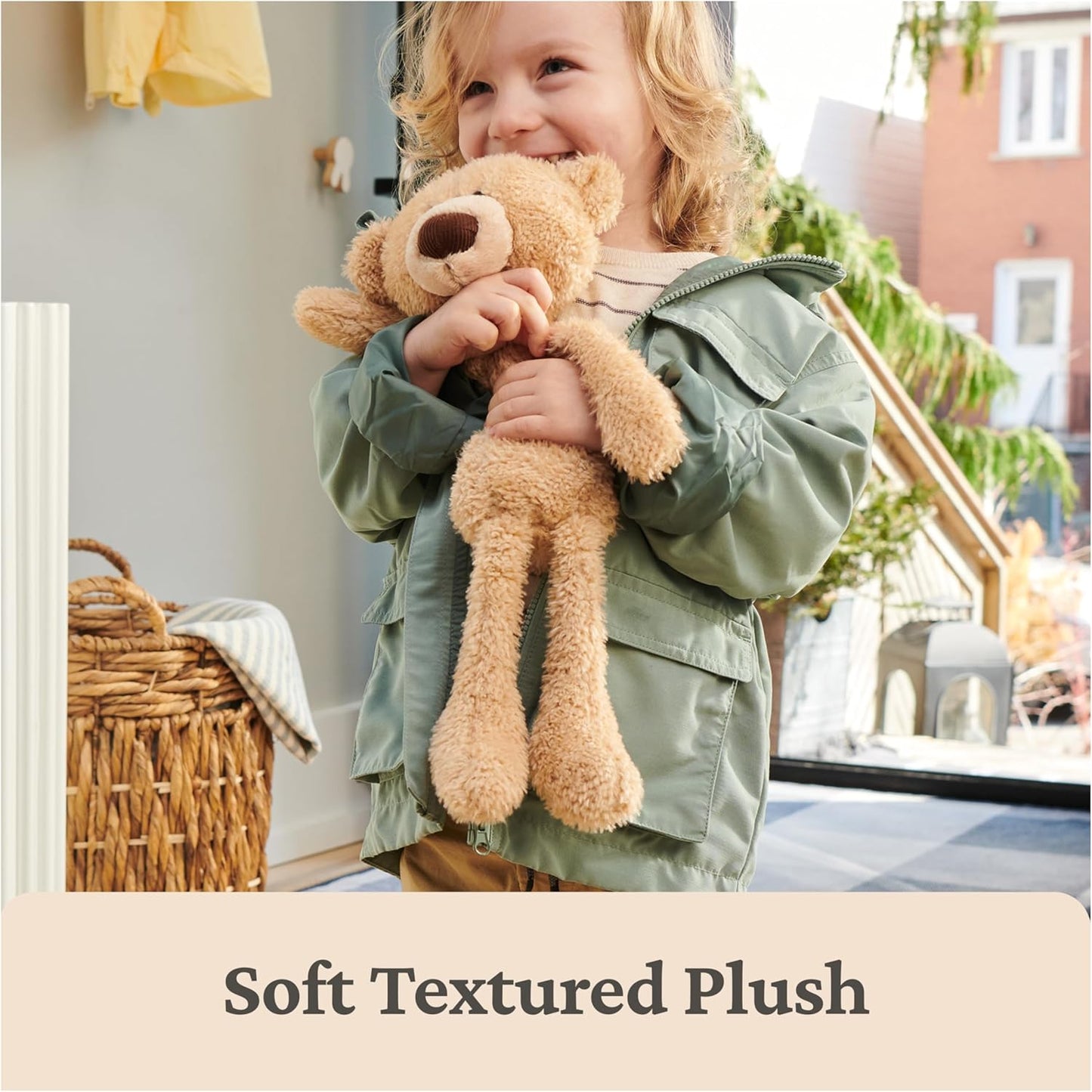 Child holding a teddy bear in a room with a basket and window in the background, text 'Soft Textured Plush' at the bottom.