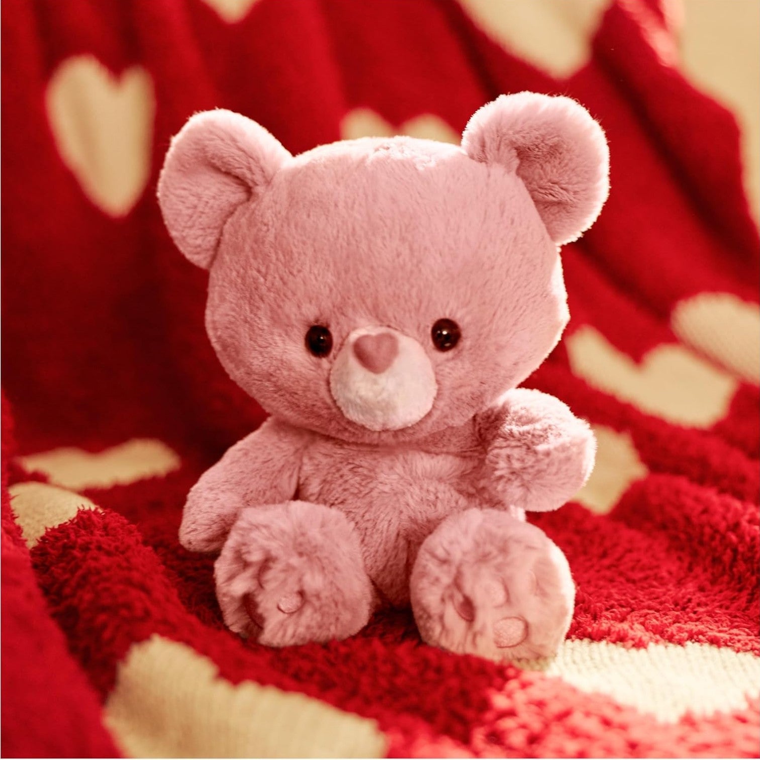 Pink teddy bear on a red blanket with heart patterns